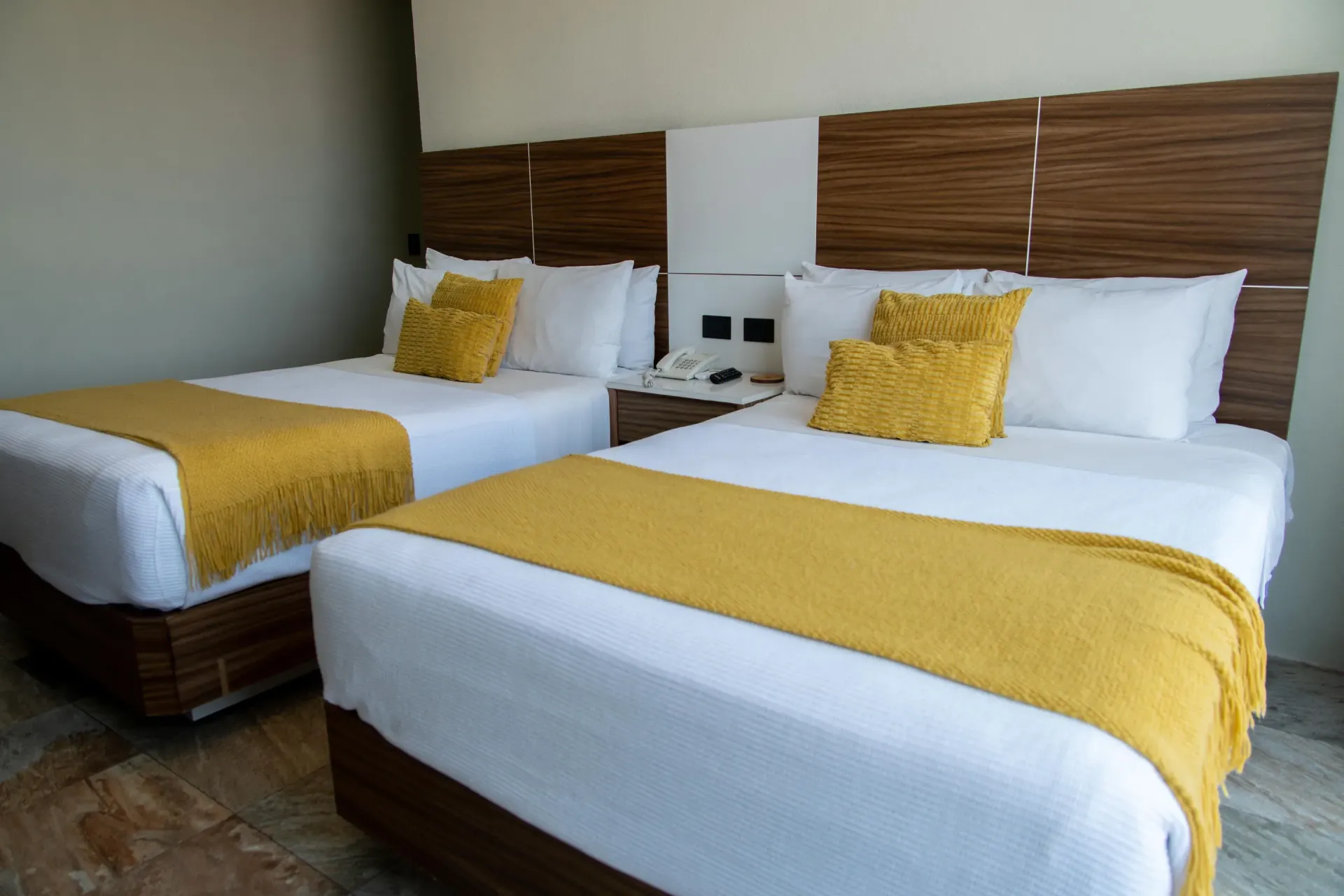 Dos camas individuales bien hechas con ropa de cama blanca y mostaza en una habitación de hotel moderna.