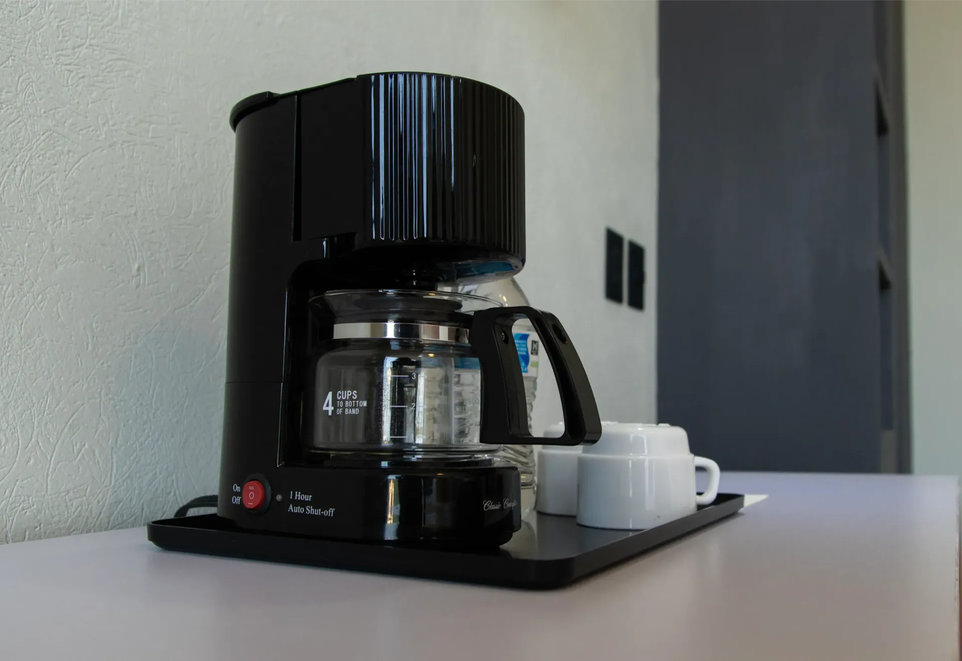 Cafetera negra sobre la encimera, junto a una taza y un platillo blancos en una cocina.