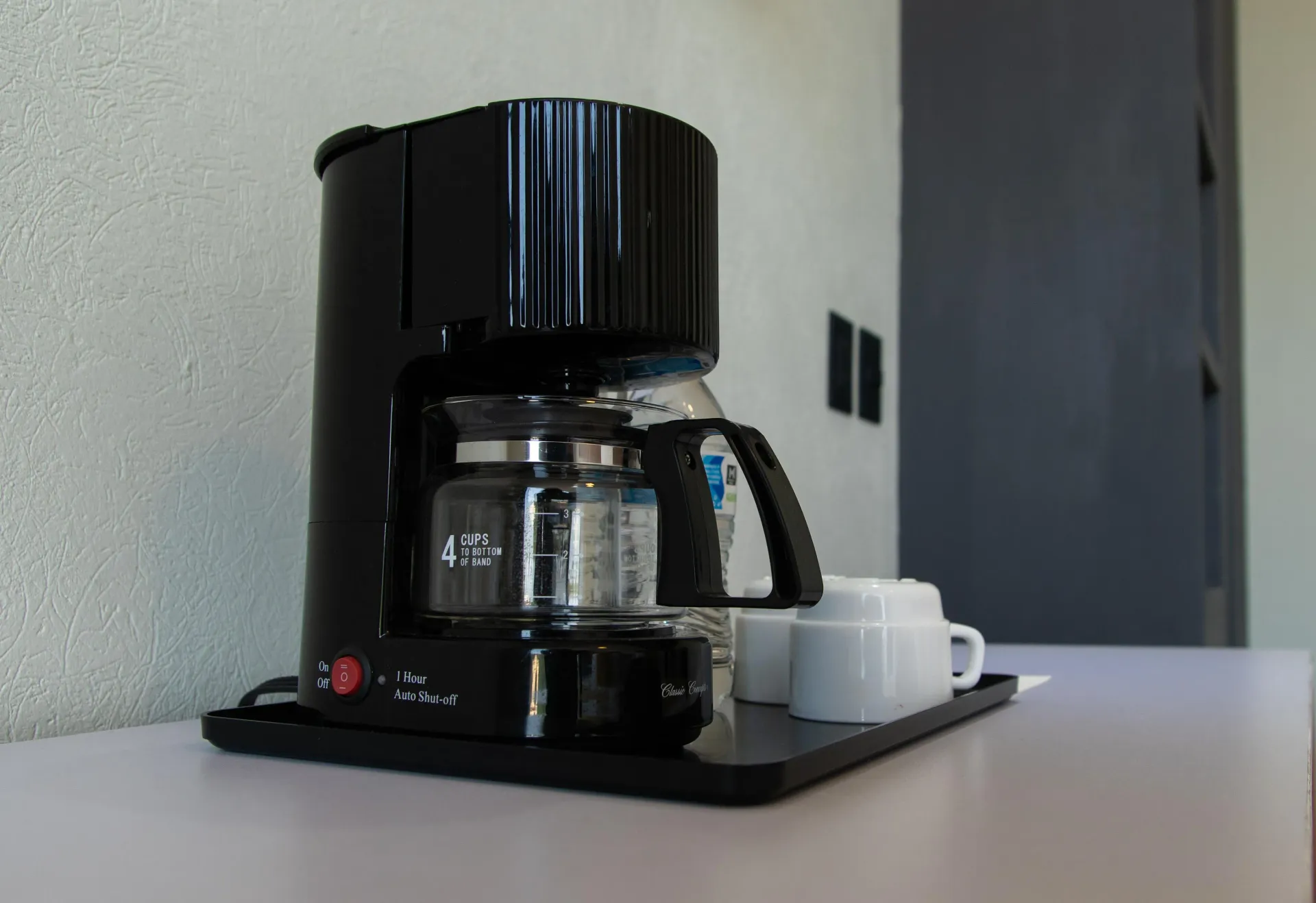 Cafetera negra preparando café sobre una encimera junto a una taza blanca en una cocina.