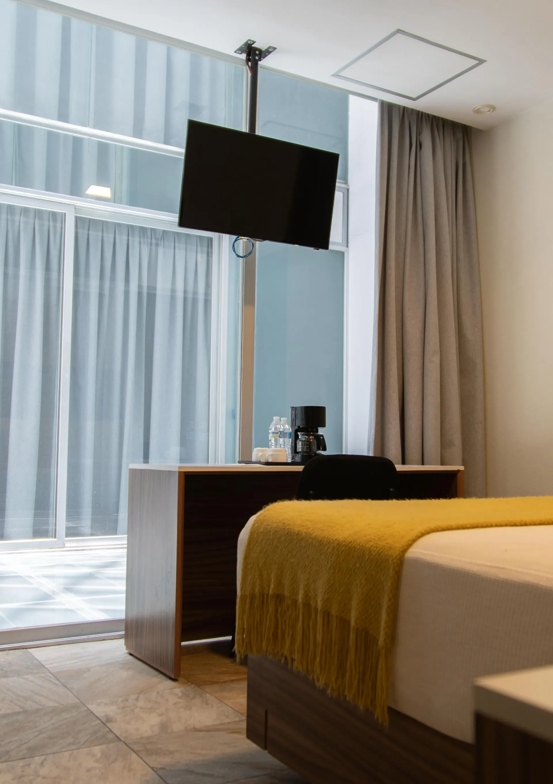 Habitación de hotel moderna con cama, escritorio, televisor de pared y ventana grande con cortinas.
