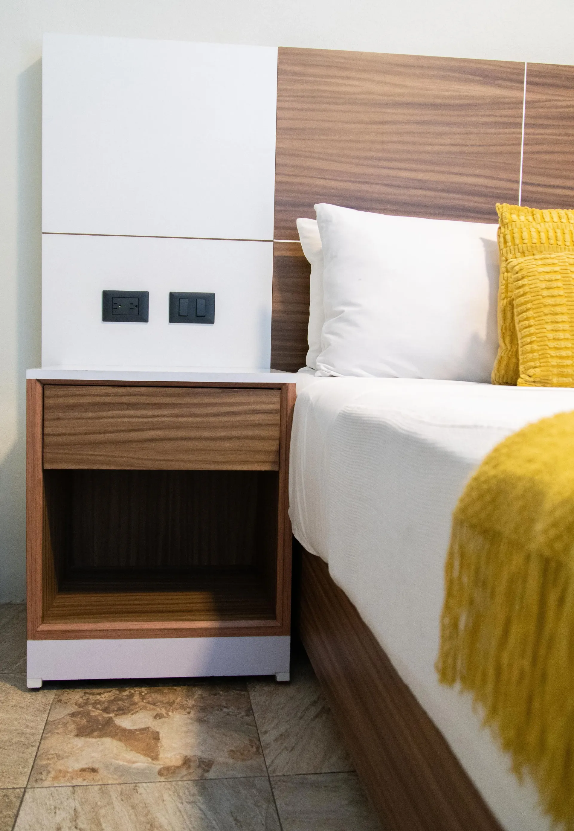 Dormitorio moderno con mesita de noche de madera, cama con almohadas blancas y una manta decorativa .