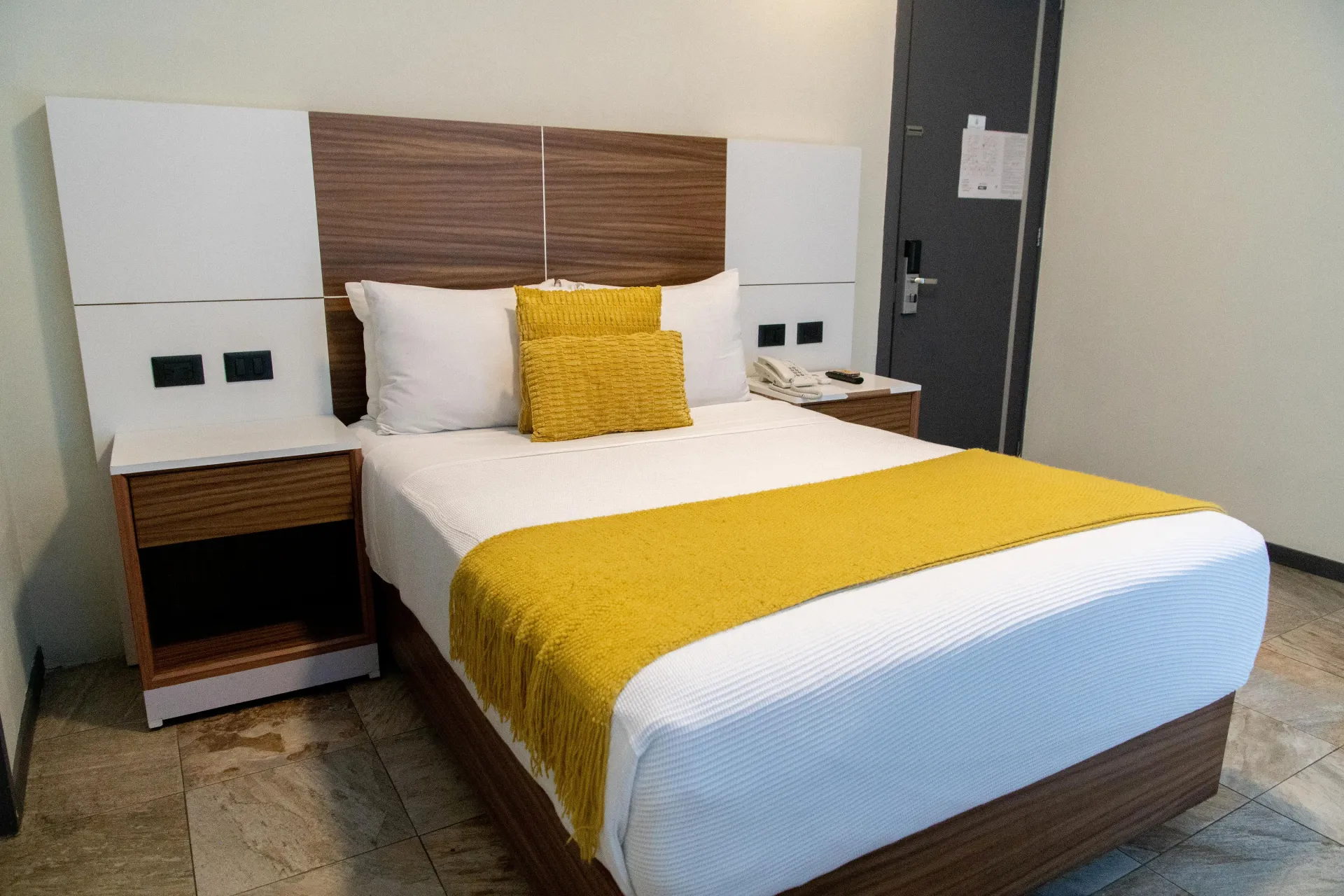 Habitación de hotel moderna con una cama bien hecha, detalles en amarillo y mesitas de noche.