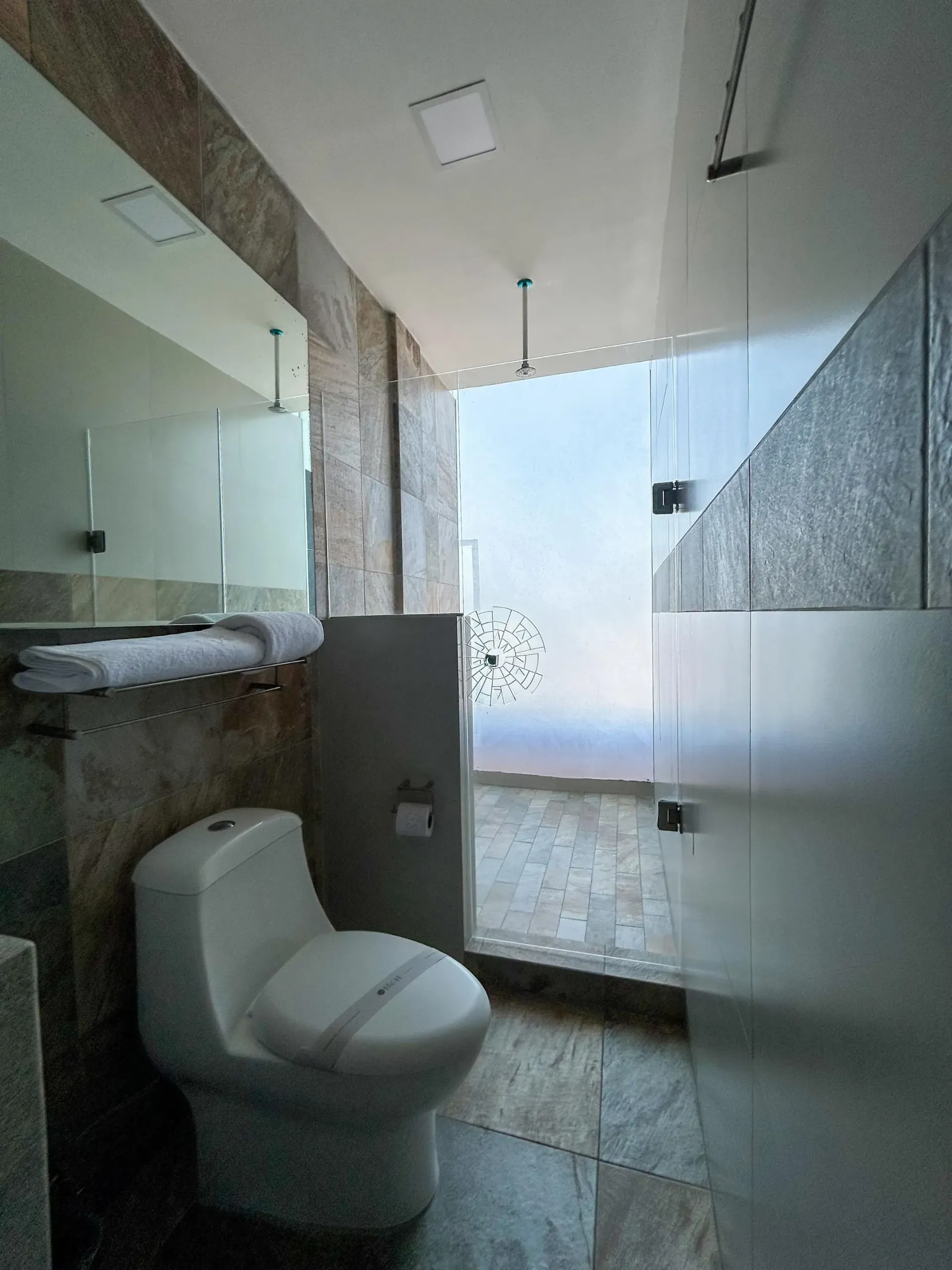Baño moderno con inodoro blanco, ducha de cristal y paredes y suelo de azulejos de mármol gris.