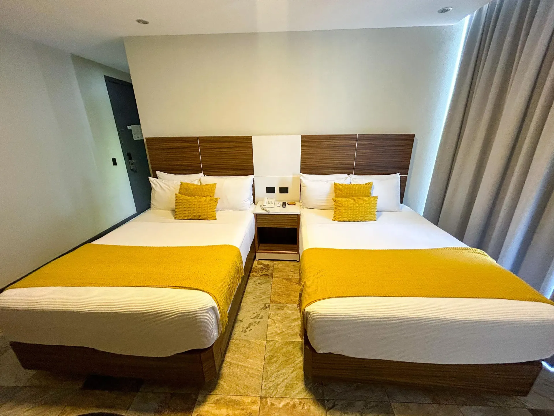 Dos camas individuales con detalles amarillos en una habitación de hotel moderna, vistas desde los pies de las camas.