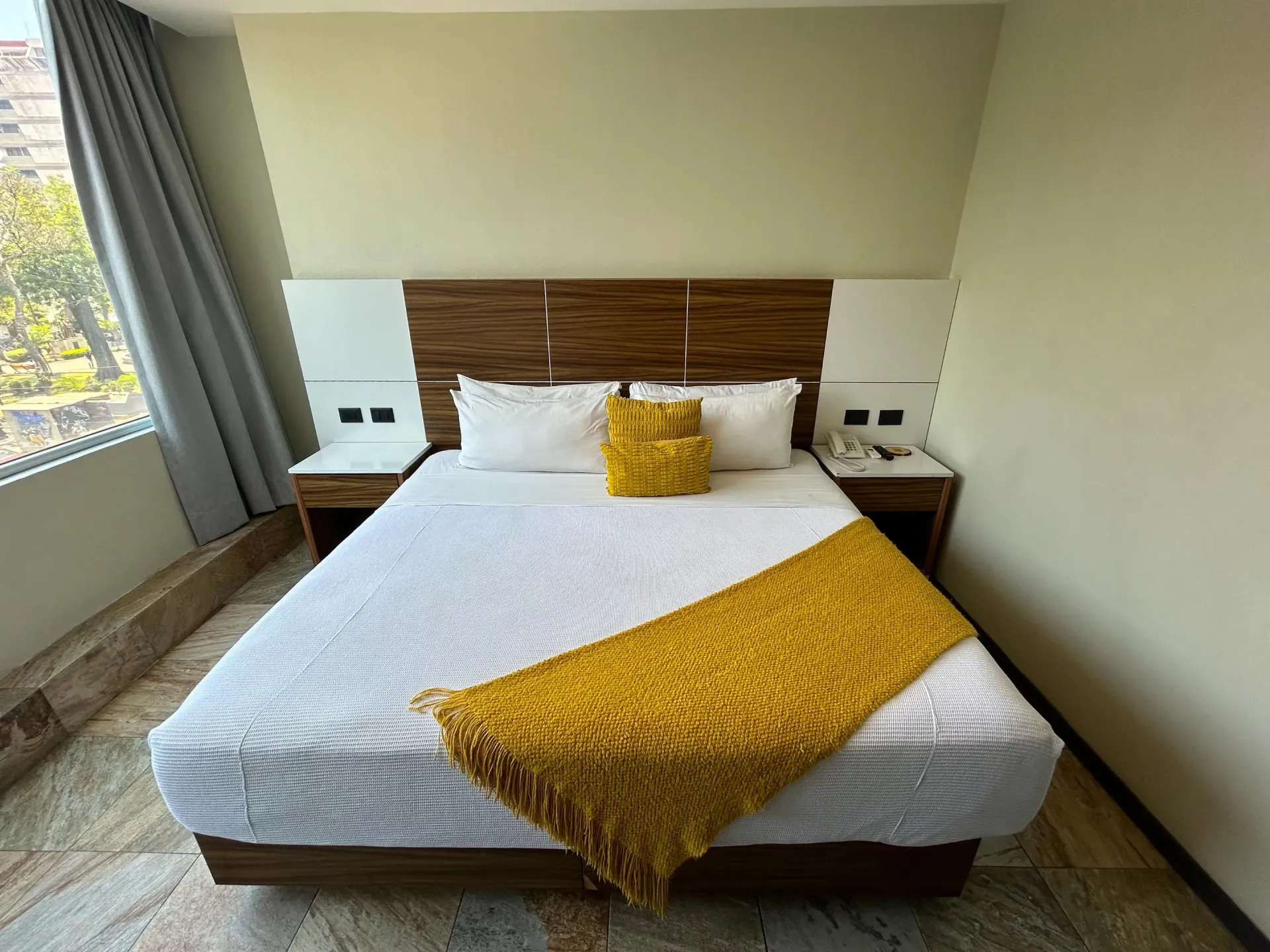 Cama bien hecha con ropa de cama blanca y detalles en amarillo en un dormitorio moderno y luminoso.