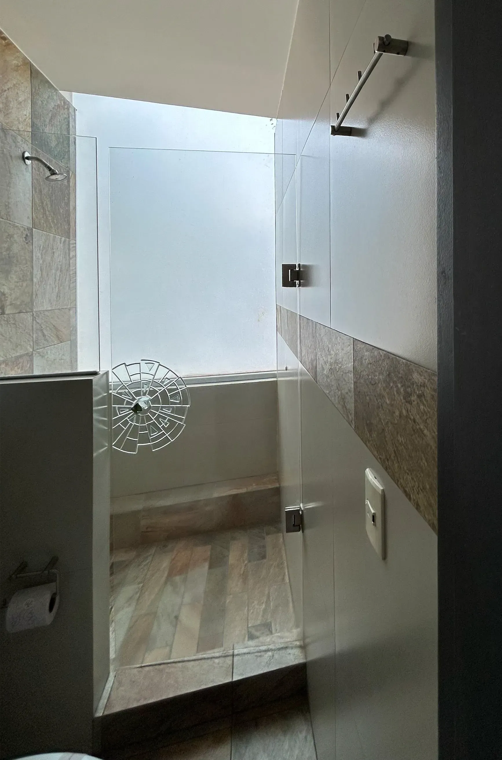 Pequeña cabina de ducha alicatada con mampara de cristal esmerilado y suelo de piedra clara.