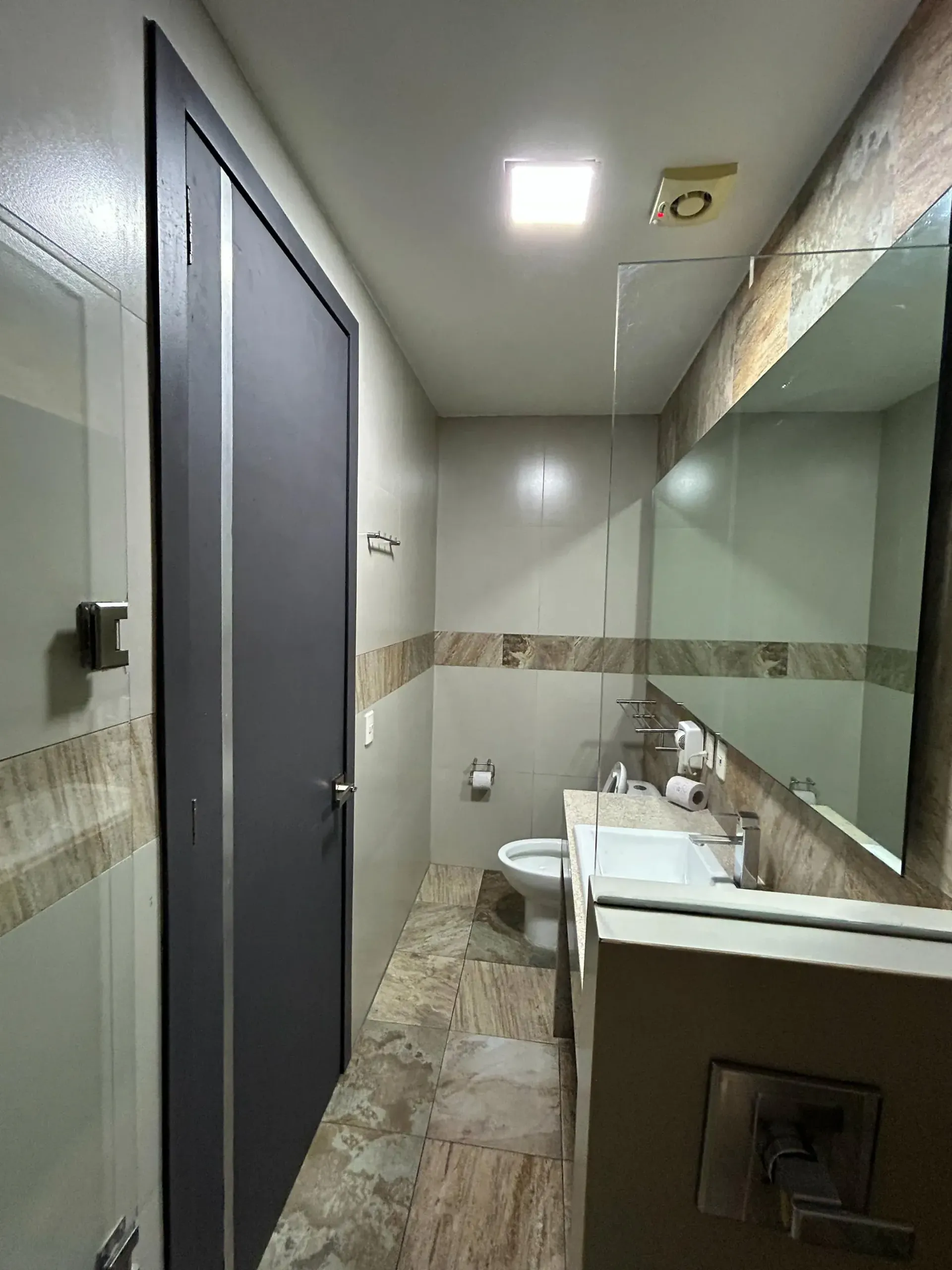 Baño moderno con puertas de cabina grises, lavabo blanco y espejo grande.