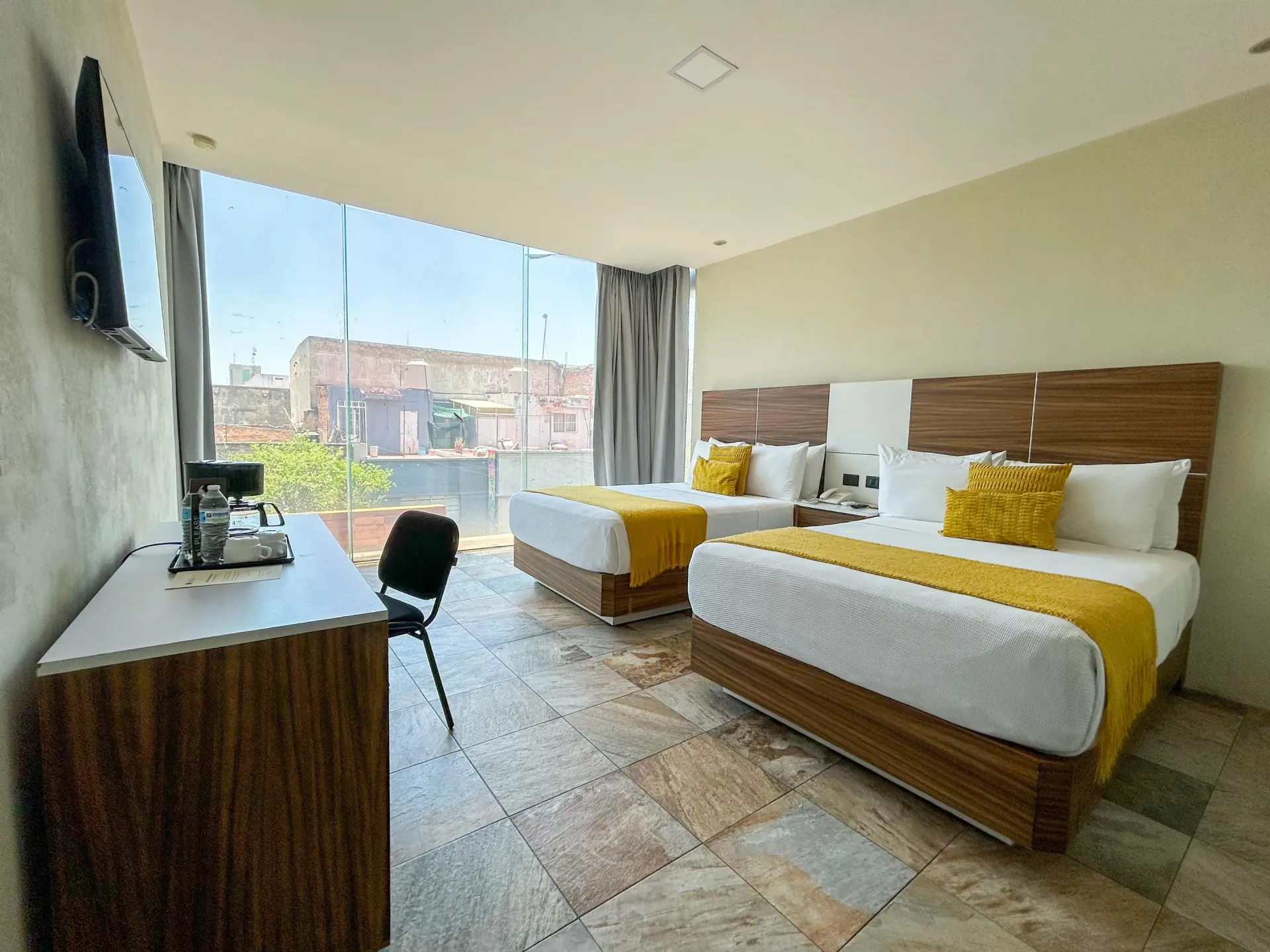 Habitación de hotel moderna con dos camas, ventana grande, escritorio y vista a la ciudad.
