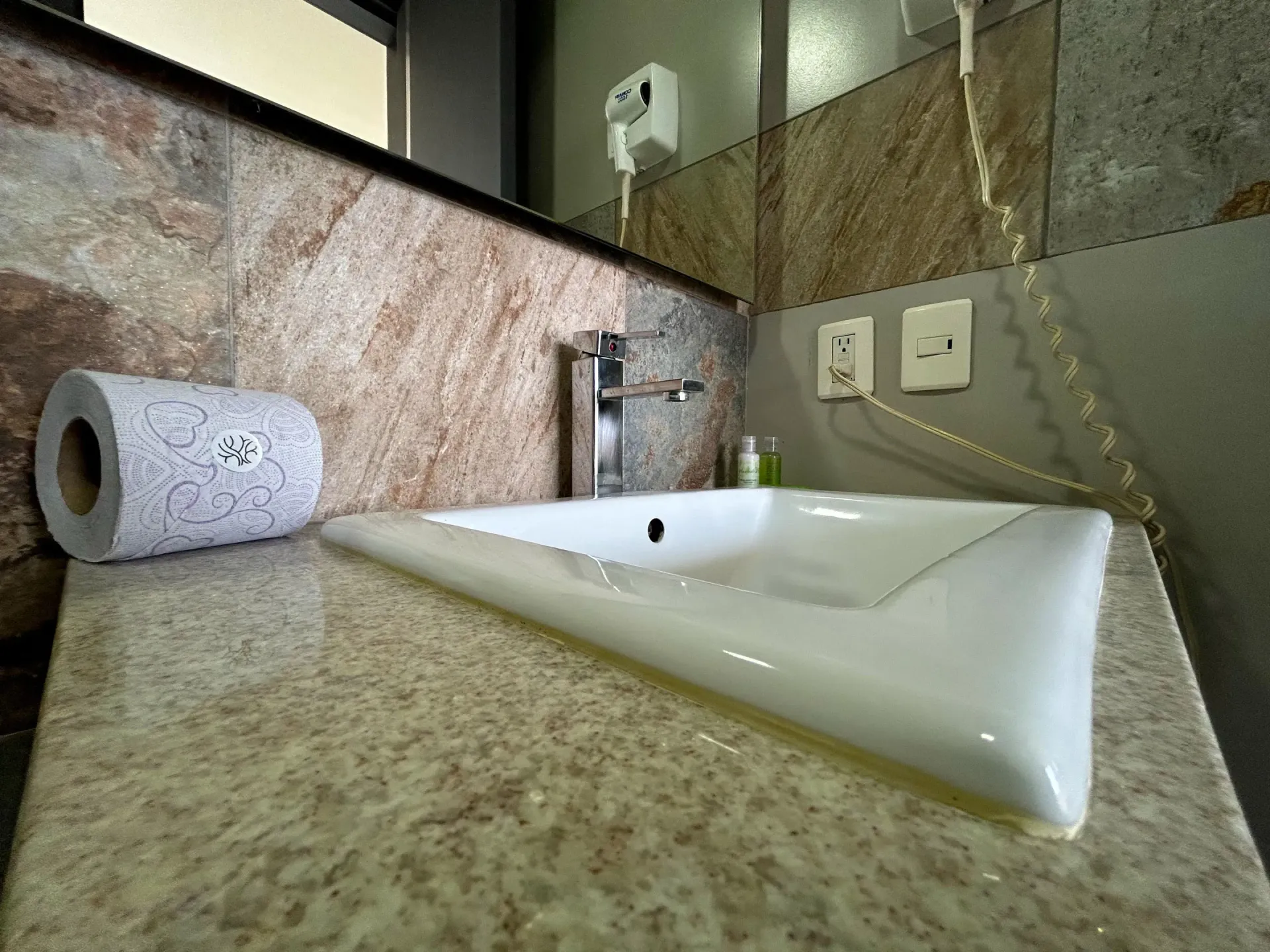Lavabo moderno con encimera de granito, espejo de pared y rollo de papel higiénico.