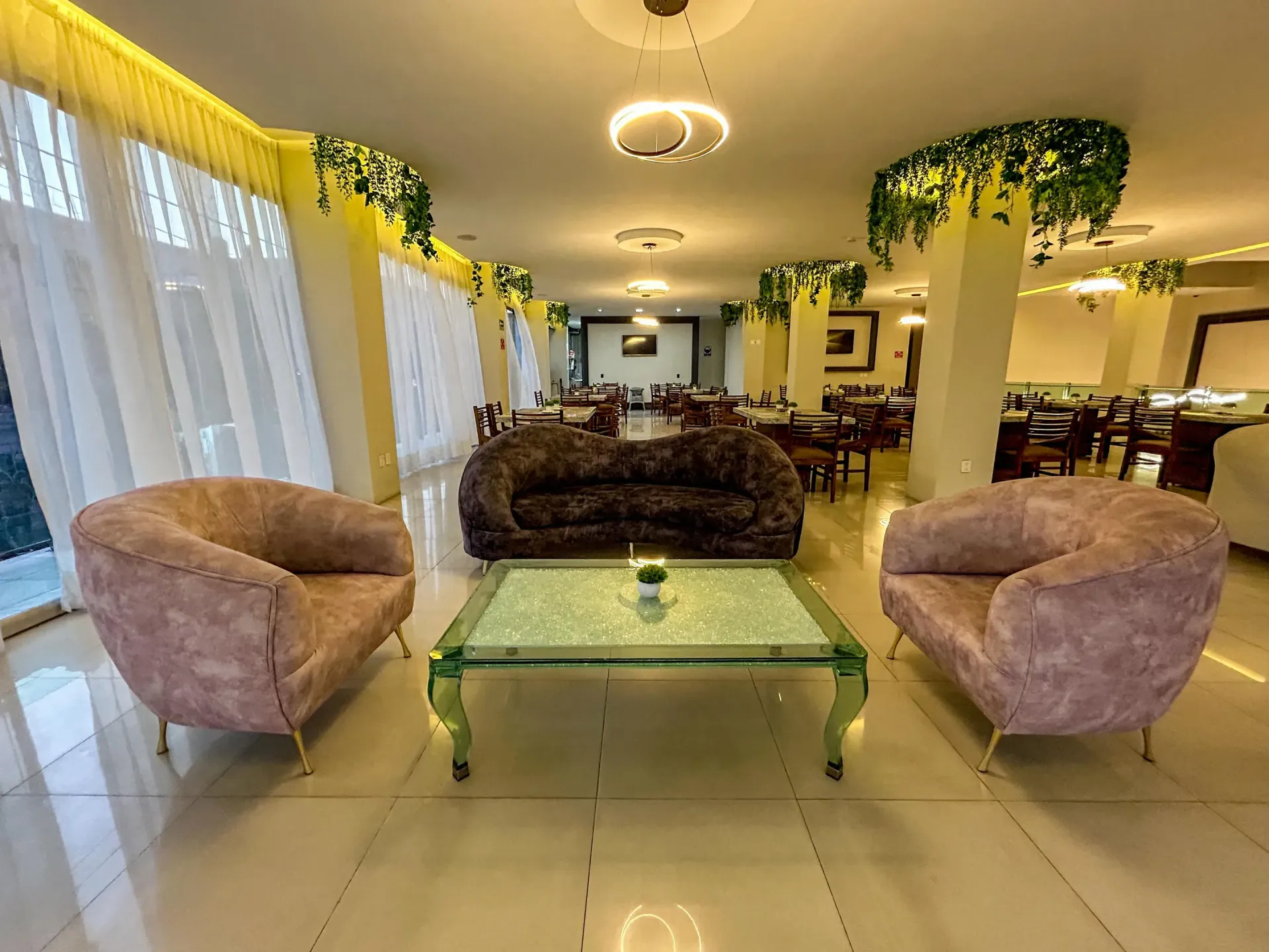 Elegante salón con sillones rosas, mesa de centro de cristal y sofás oscuros en una habitación luminosa iluminada.