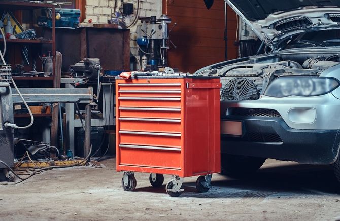 Red tool chest in a cluttered auto garage beside a silver car with the hood open