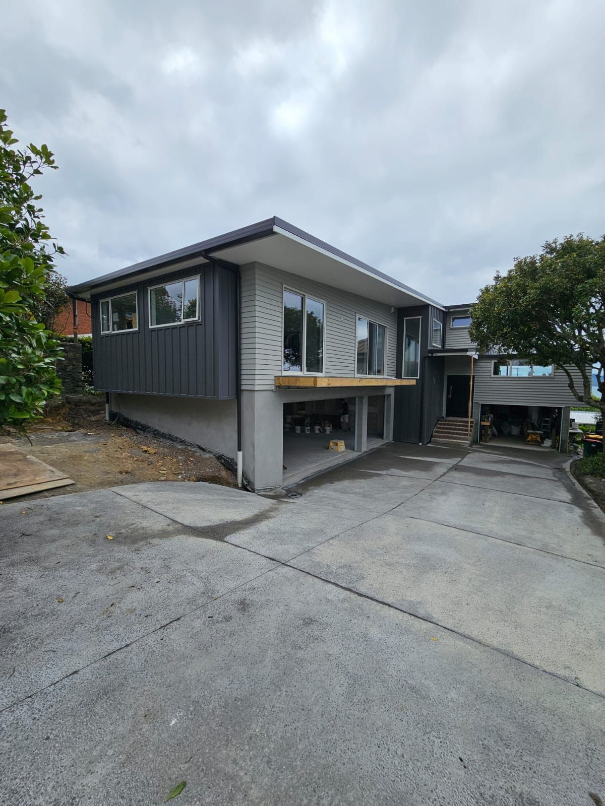 Modern two-story house with gray and dark gray siding. Concrete driveway. Cloudy sky.