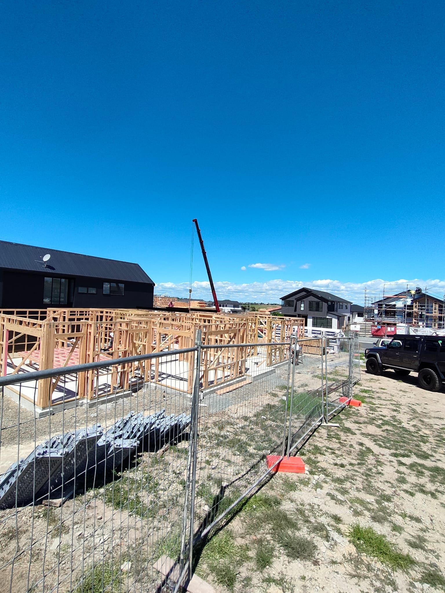 Construction site with wooden frames, crane, and completed houses under a blue sky.