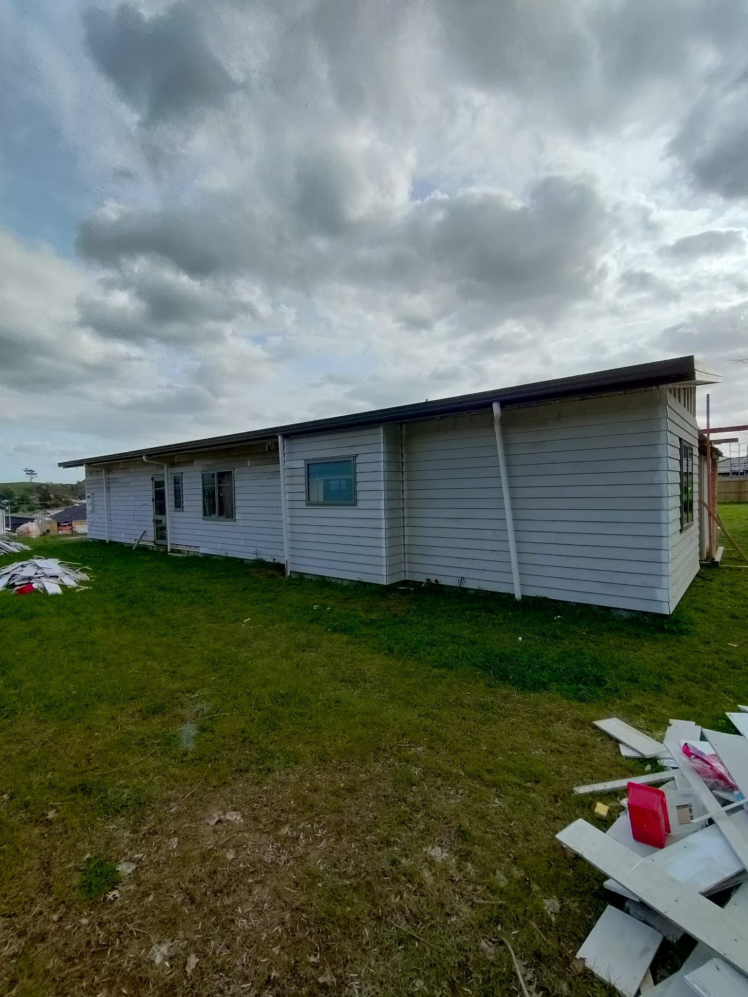 White building with dark roof, under cloudy sky, on grassy lot.