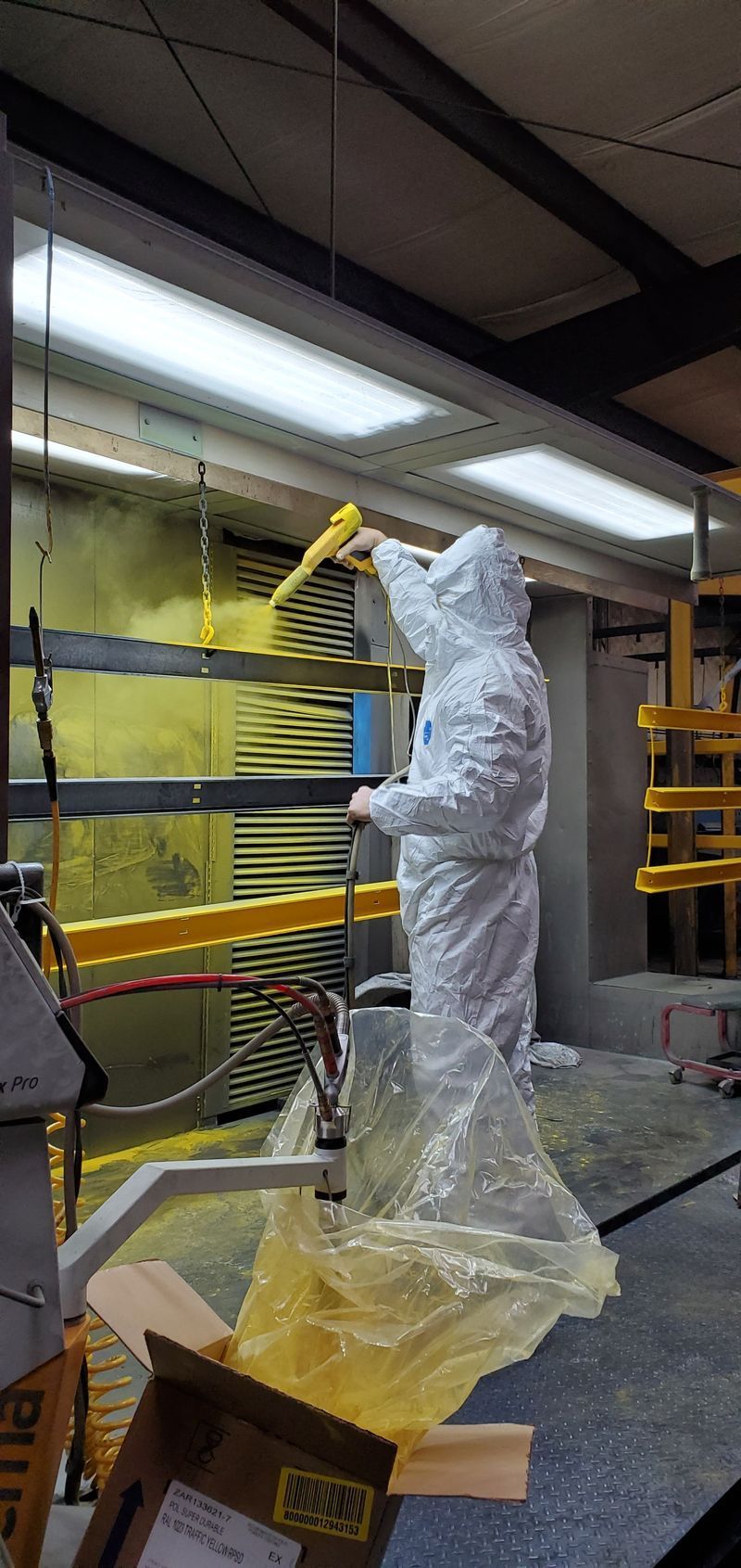 A Man in a Protective Suit is Painting a Piece of Metal in a Factory