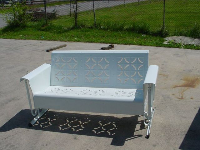 A White Bench With a Pattern on the Back Sits in a Parking Lot