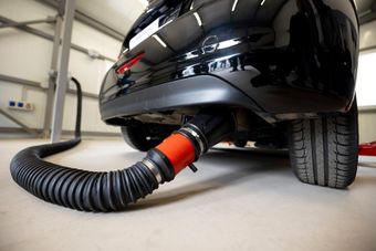 Black car connected to a red-and-black hose in a garage, likely for exhaust or vacuum testing | Cain And Sons' Automotive