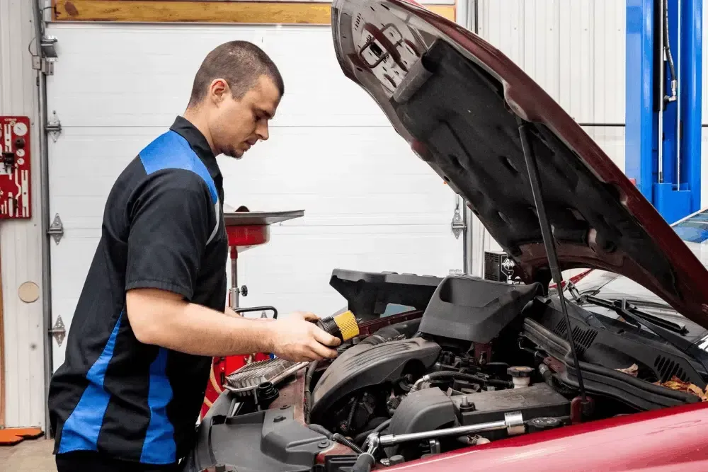 Mechanic inspecting a red car engine with the hood open in an auto shop | Cain And Sons' Automotive