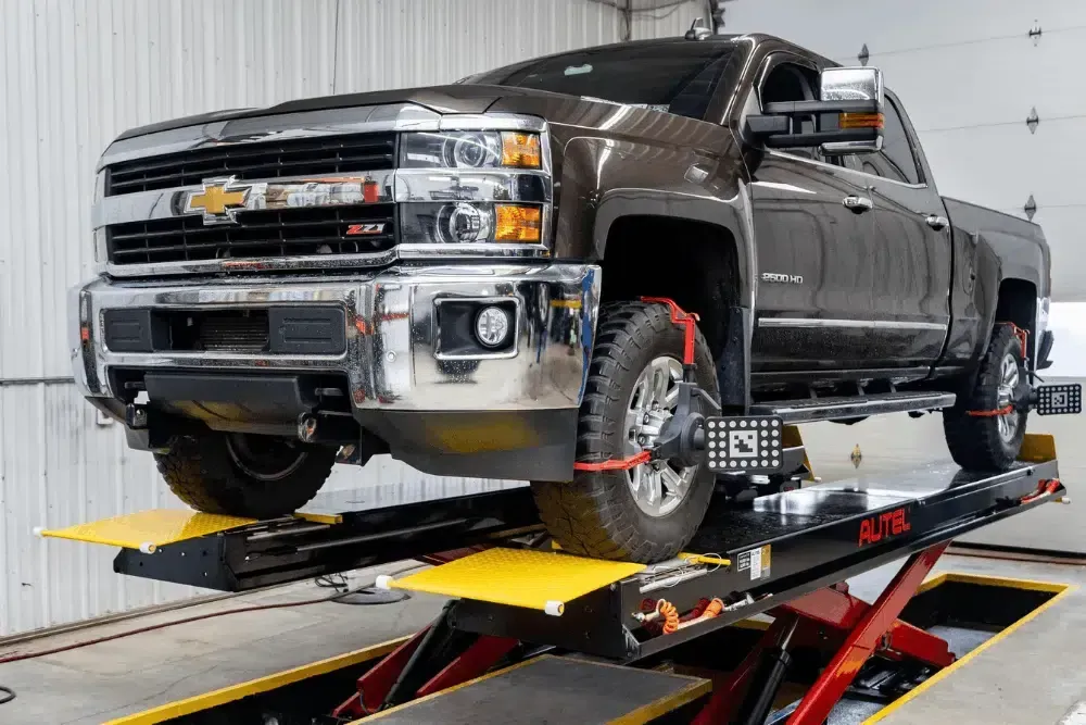 Brown Chevrolet pickup on a vehicle lift in an auto shop, with red wheel restraints and yellow platforms | Cain And Sons' Automotive