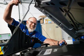 Mechanic in blue shirt inspecting a car engine with the hood open in a garage | Cain And Sons' Automotive