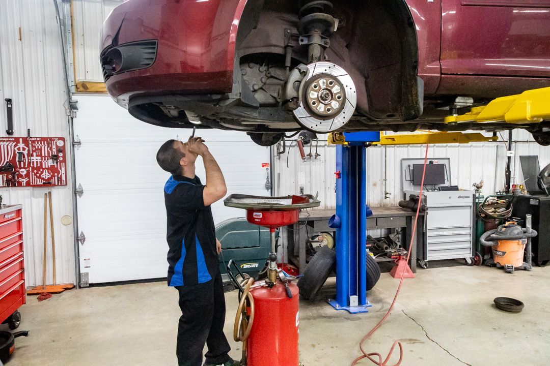 Mechanic working under a red car on a lift in an auto repair shop | Cain And Sons' Automotive
