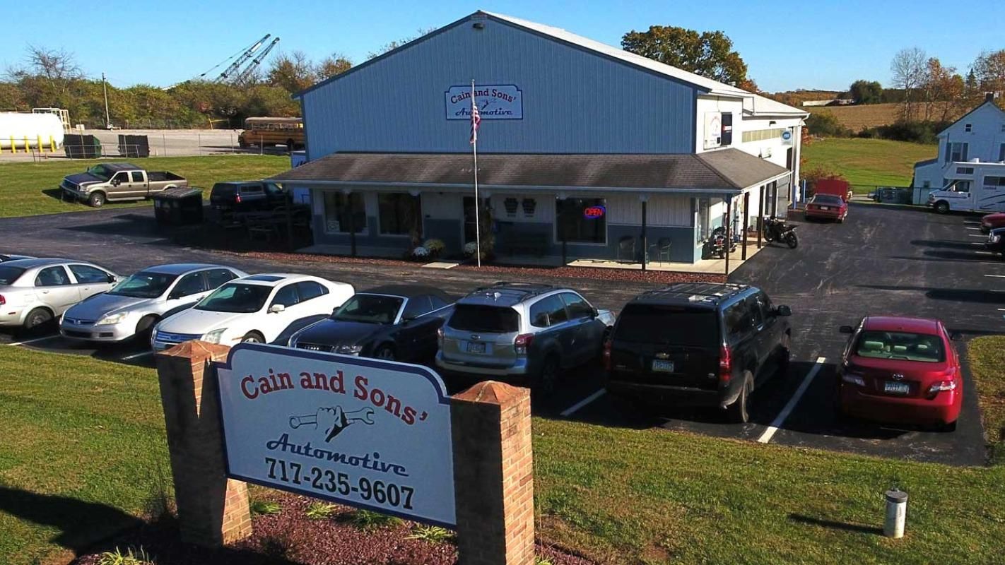 Exterior of a hotel with parked cars and a roadside sign in front, under a clear sky | Cain And Sons' Automotive