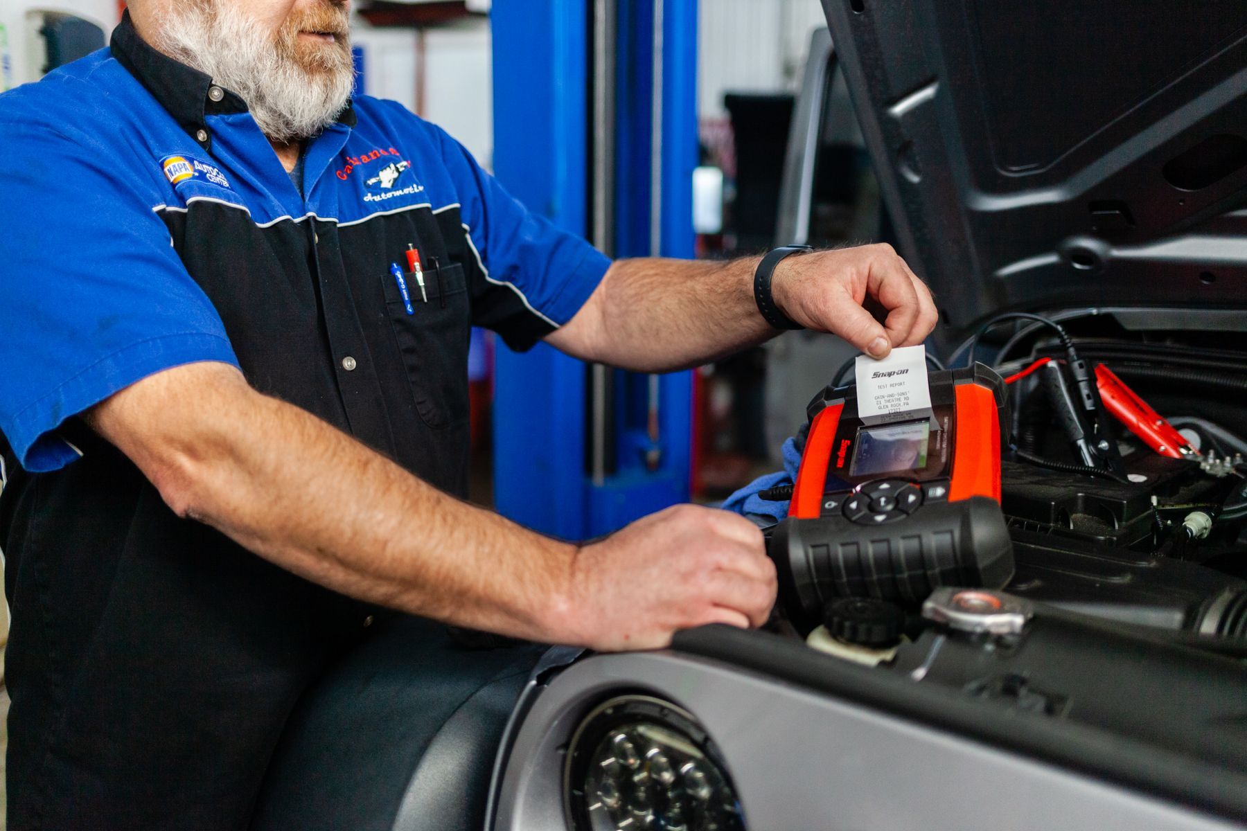 Mechanic in blue uniform checking a car battery in an auto repair shop| Cain And Sons' Automotive