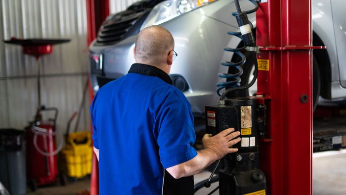Mechanic in blue shirt inspecting a car on a lift in an auto repair shop | Cain And Sons' Automotive