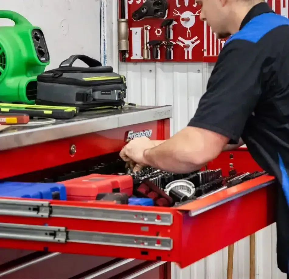 Mechanic organizing tools in an open red toolbox beside a workbench. | Cain And Sons' Automotive