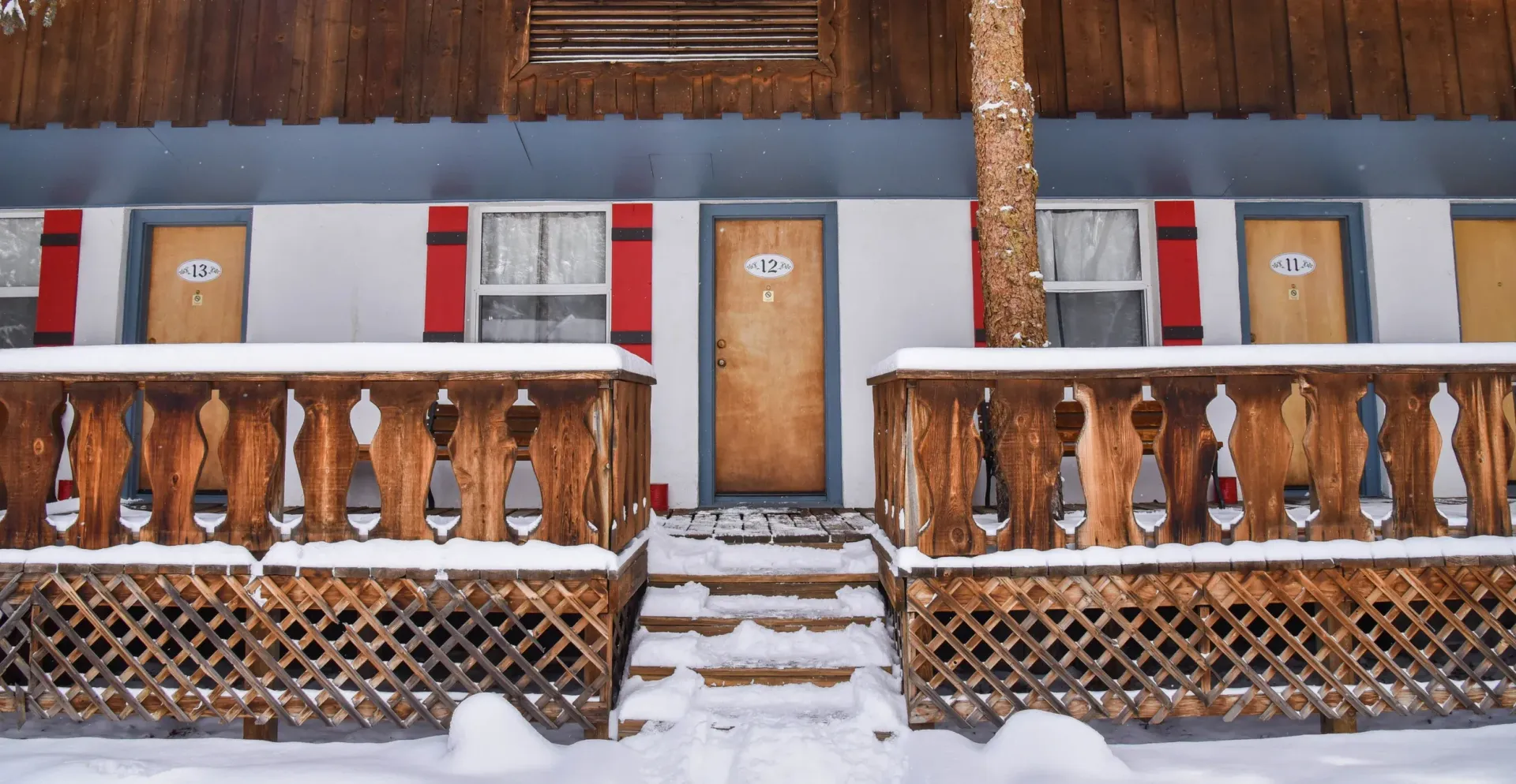 A snowy motel in winter, with wooden porch railing, doors, and red shutters.