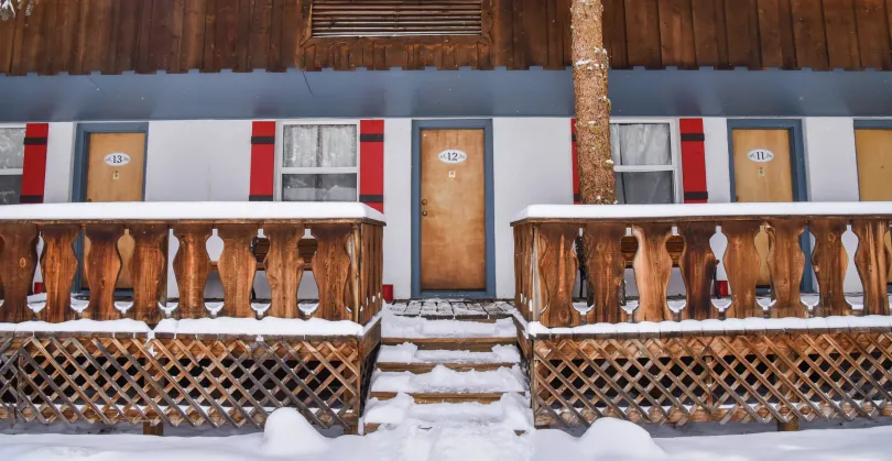 A snowy motel in winter, with wooden porch railing, doors, and red shutters.