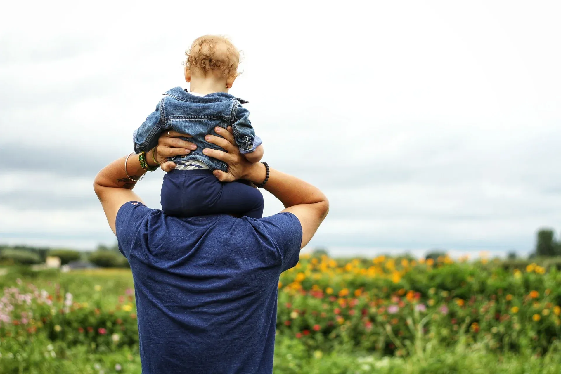 A man is carrying a baby on his shoulders in a field.