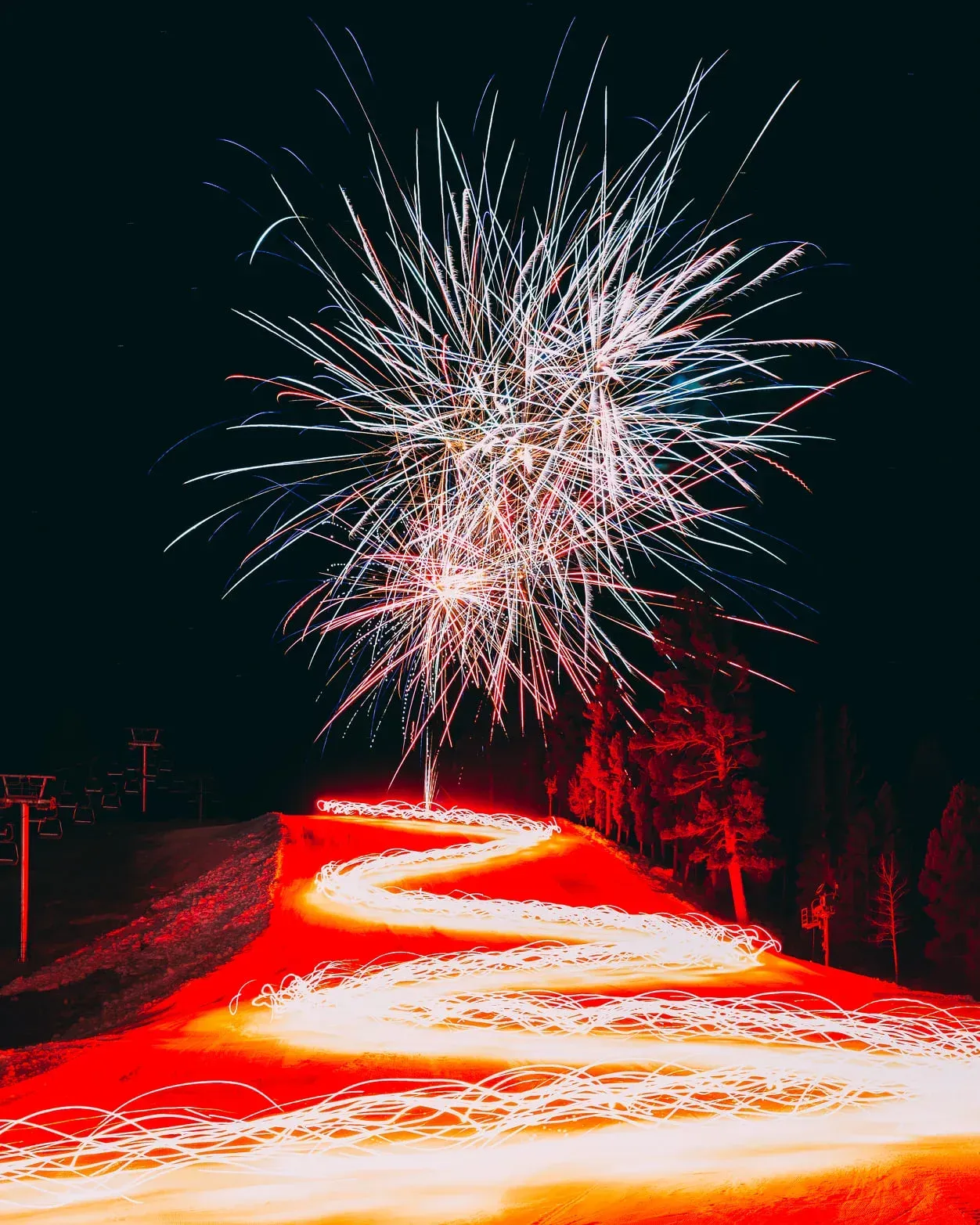 Fireworks are displayed over a snowy slope at night