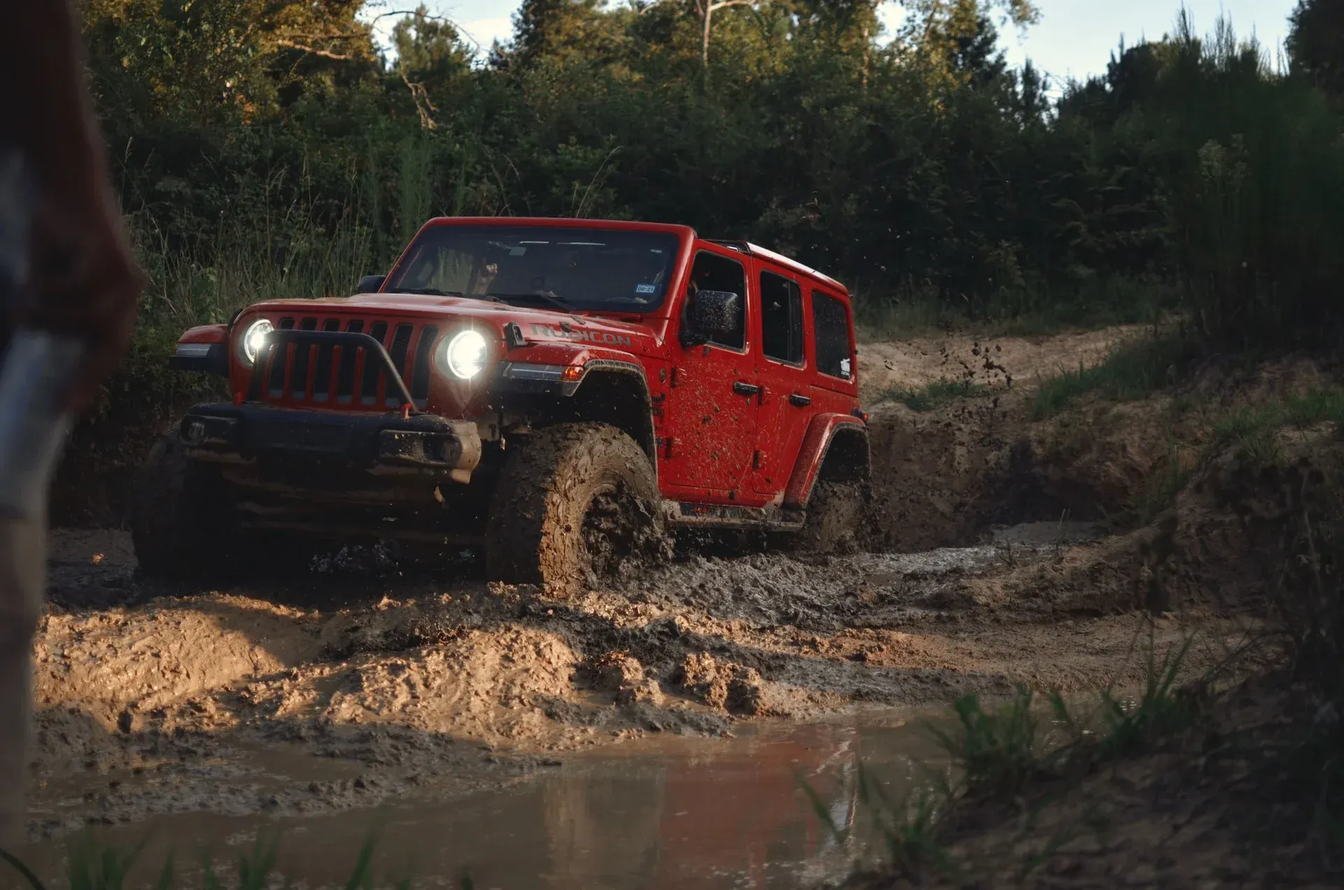 A red jeep is driving through a muddy area.