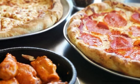 Three pizzas and a bowl of buffalo wings are on a table.