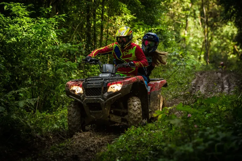 A man and a woman are riding an atv through the woods.