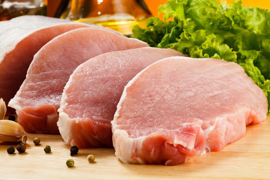 Bistecche di maiale crude su un tagliere con erbe aromatiche e grani di pepe.