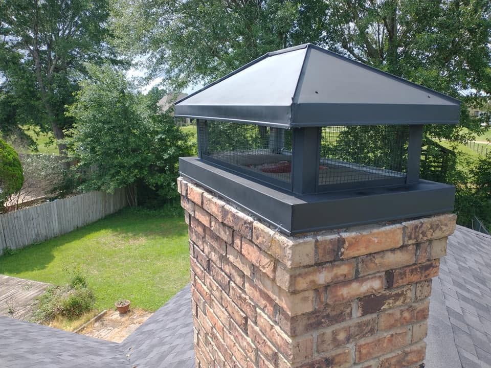 Backyard brick chimney with a gray metal cap beside a lawn and fence