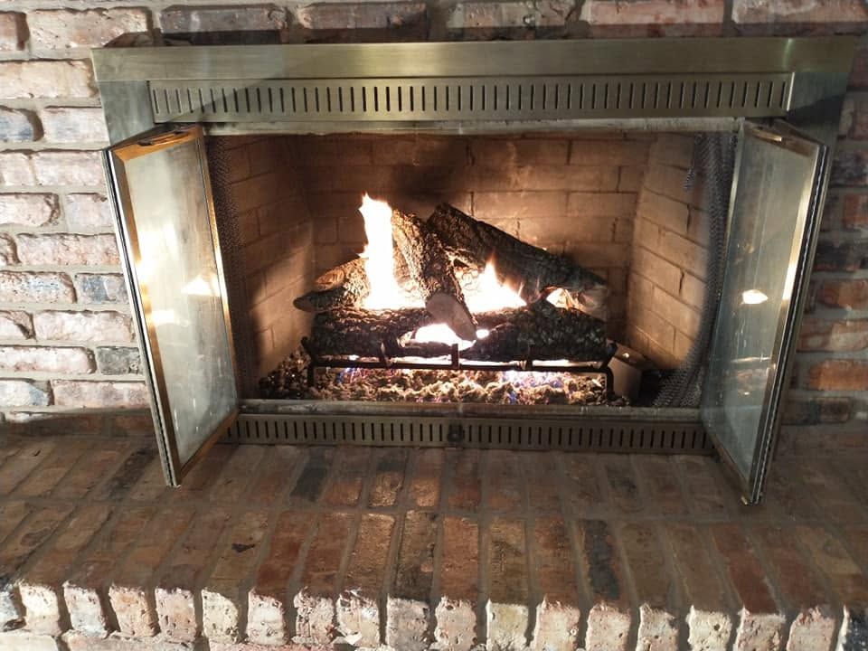 Lit brick fireplace with glass doors and a burning fire inside