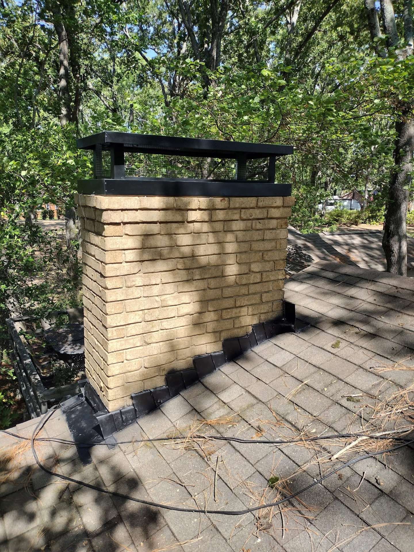 Brick outdoor trash bin with black lid on a paved path in a wooded area