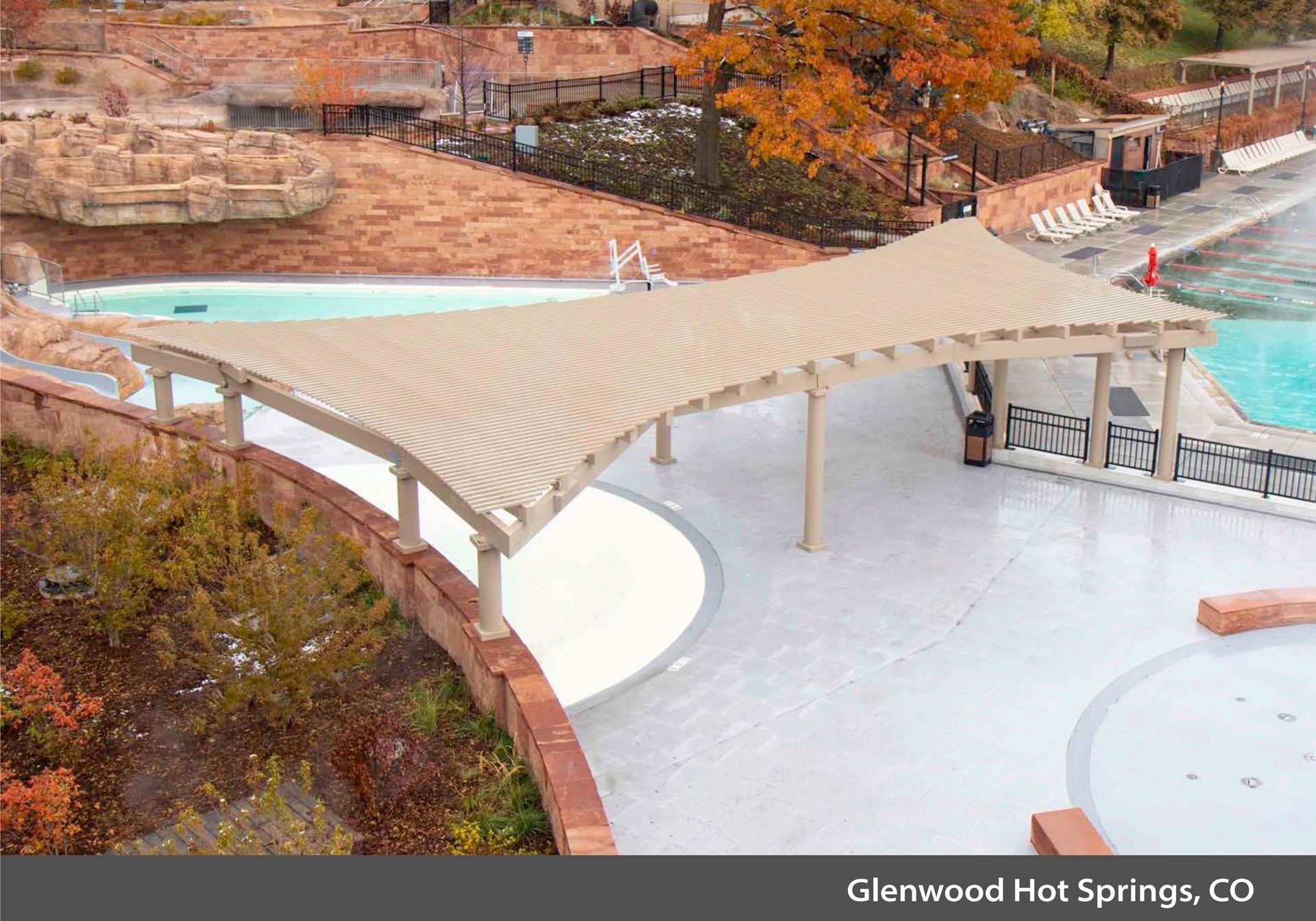 Aerial view of a tan shade canopy over a white pool deck at Glenwood Hot Springs, with autumn trees nearby