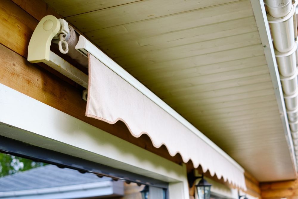 Beige retractable awning mounted above a window under a house eave