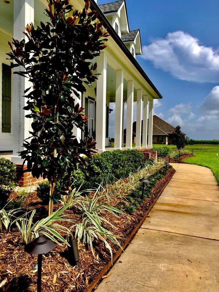 White house porch with columns beside a mulched garden bed and curving sidewalk under a blue sky.