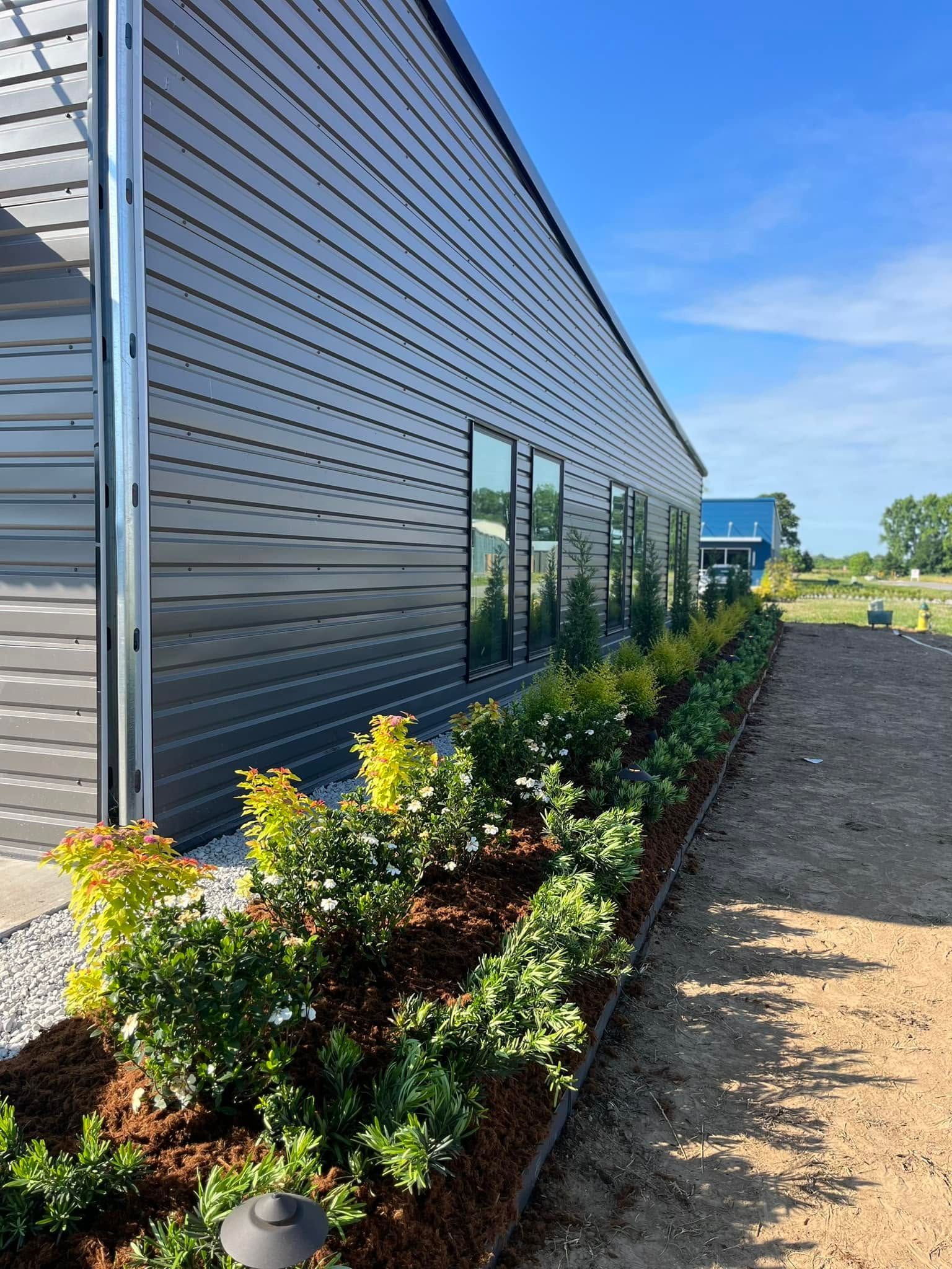 Modern gray building with reflective windows and landscaped shrubs along a gravel path under a blue sky