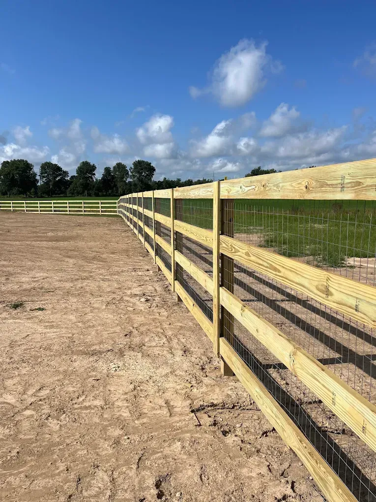 Wooden fence along a dirt paddock under a blue sky with clouds