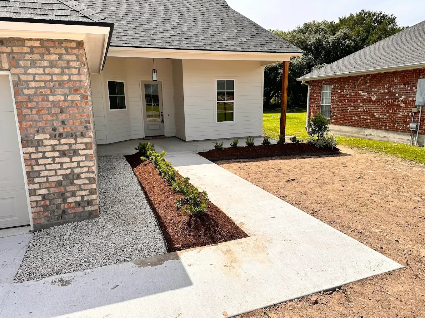 Front entrance of a house with a white walkway, brick siding, and a mulched planting bed
