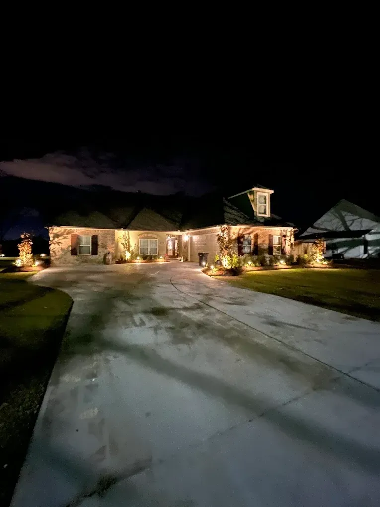 Snowy driveway leading to a warmly lit house decorated with holiday lights at night