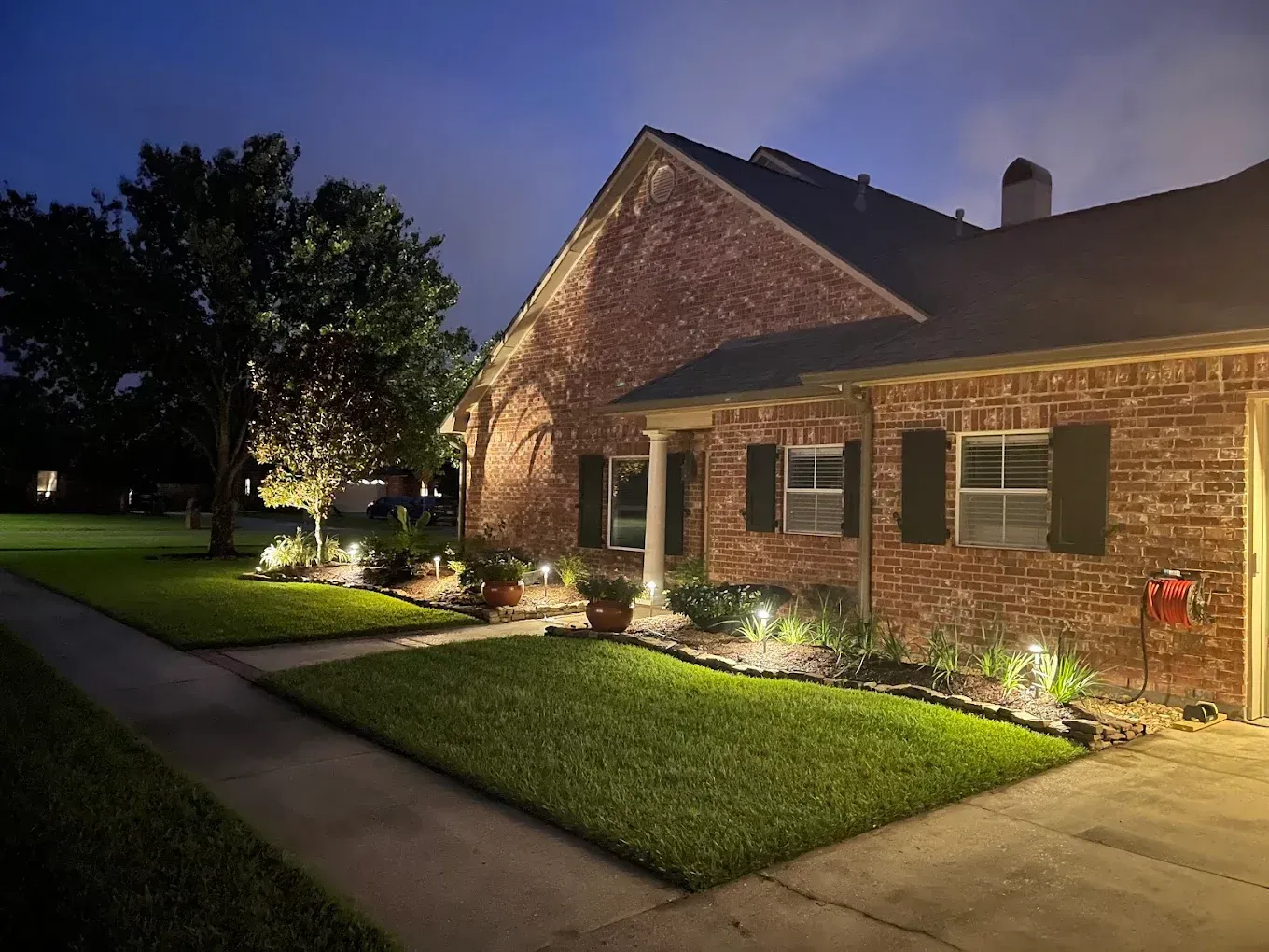Brick house exterior at dusk with lit walkway, manicured lawn, and warm porch lights