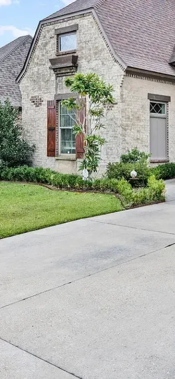 Stone house with steep roof, red front door, and a small front garden beside a driveway