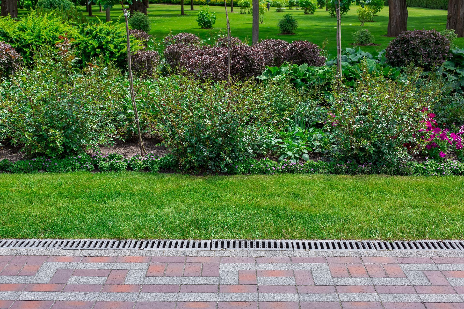 Green garden beds with shrubs and flowers beside a brick walkway